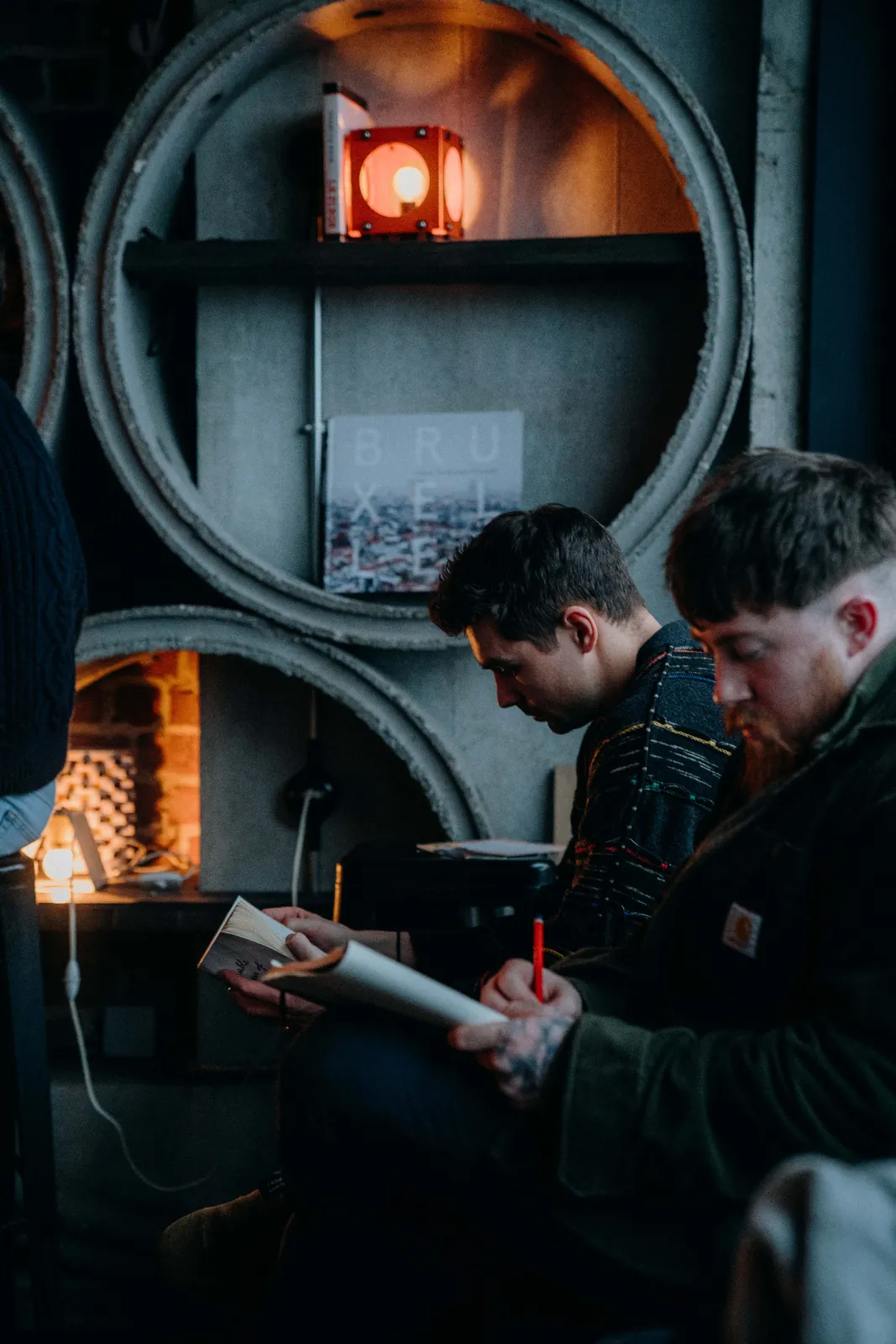 Two participants write in notebooks beside a fireplace.