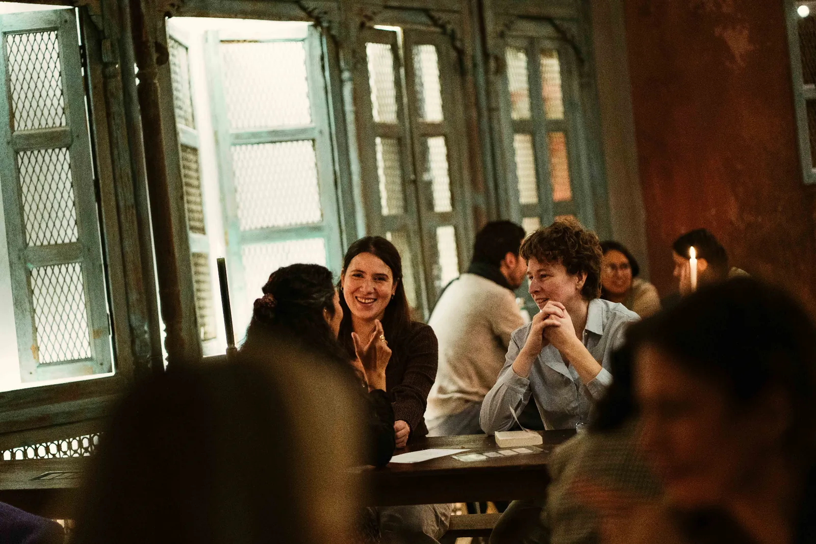Participants talk around tables in a bar beside large windows.