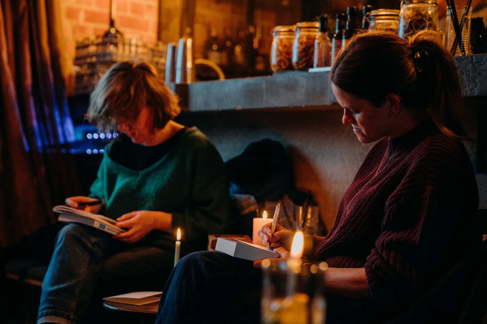 Two people read and write in notebooks by candlelight.