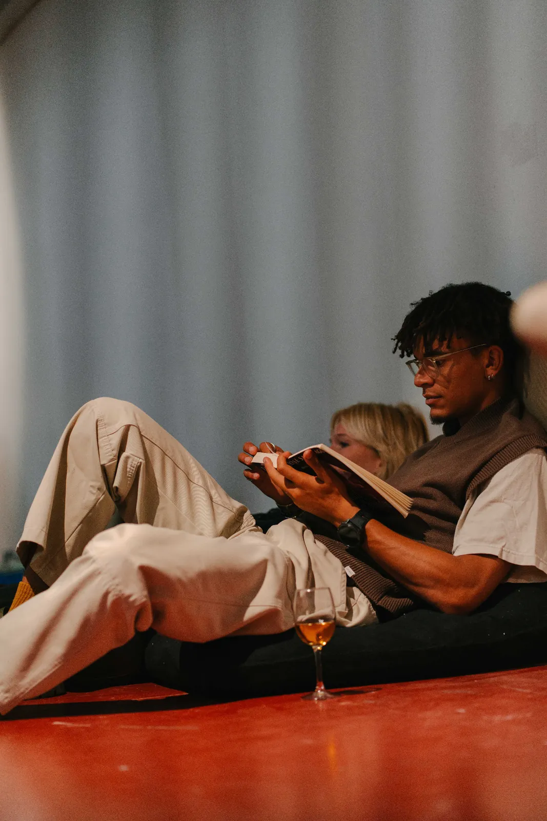 A participant reads on the floor, leaning against a light wall.